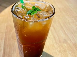 Photo: A single glass of iced tea with mint and a green straw sits on a…