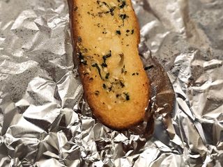 Photo: A single slice of garlic bread resting on silver foil, taken near a…