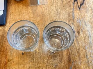 Photo: Two glasses of water on a wooden table, with a container holding…